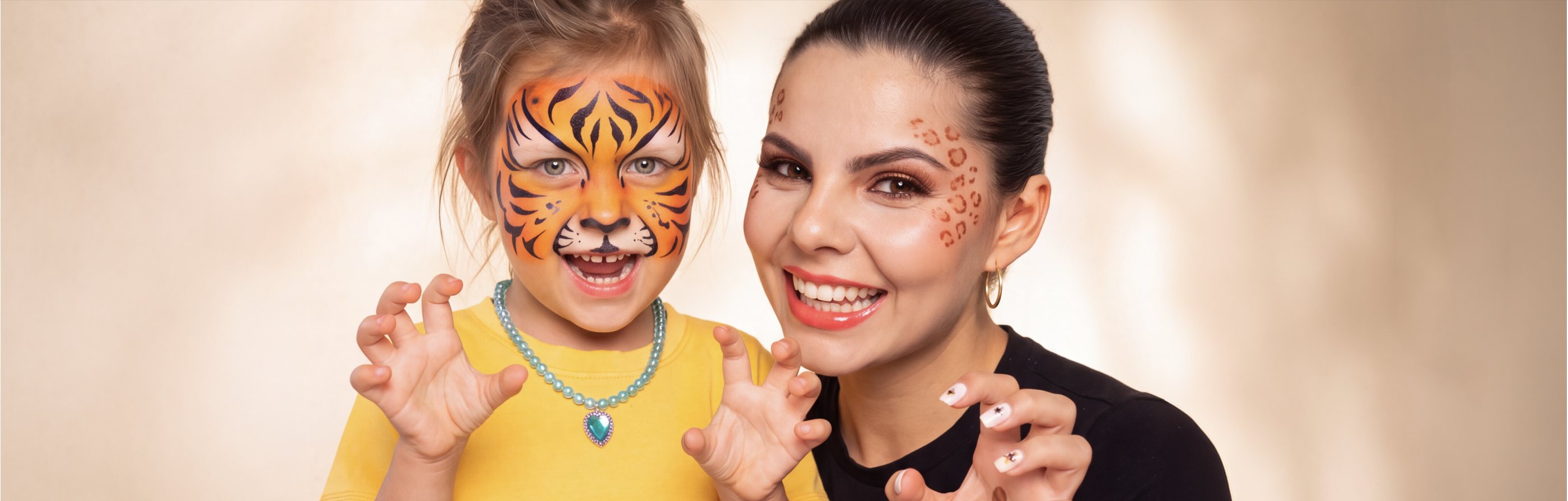 A child with tiger face paint and a woman with leopard print face paint, smiling together